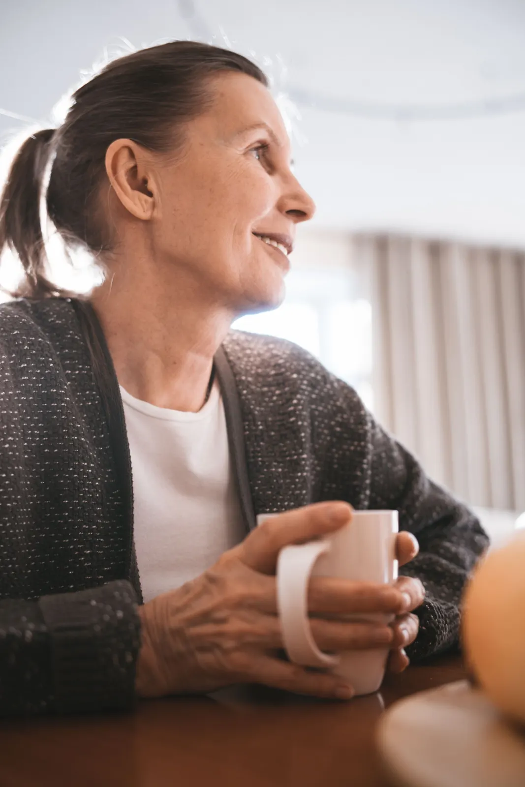 An older woman smiling with a cup of coffee at home
