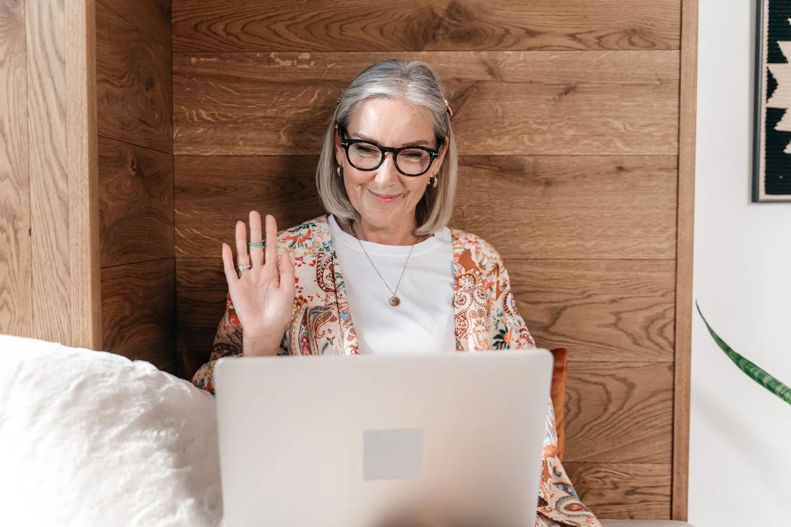 An older woman smiling and waving during a video call on her laptop
