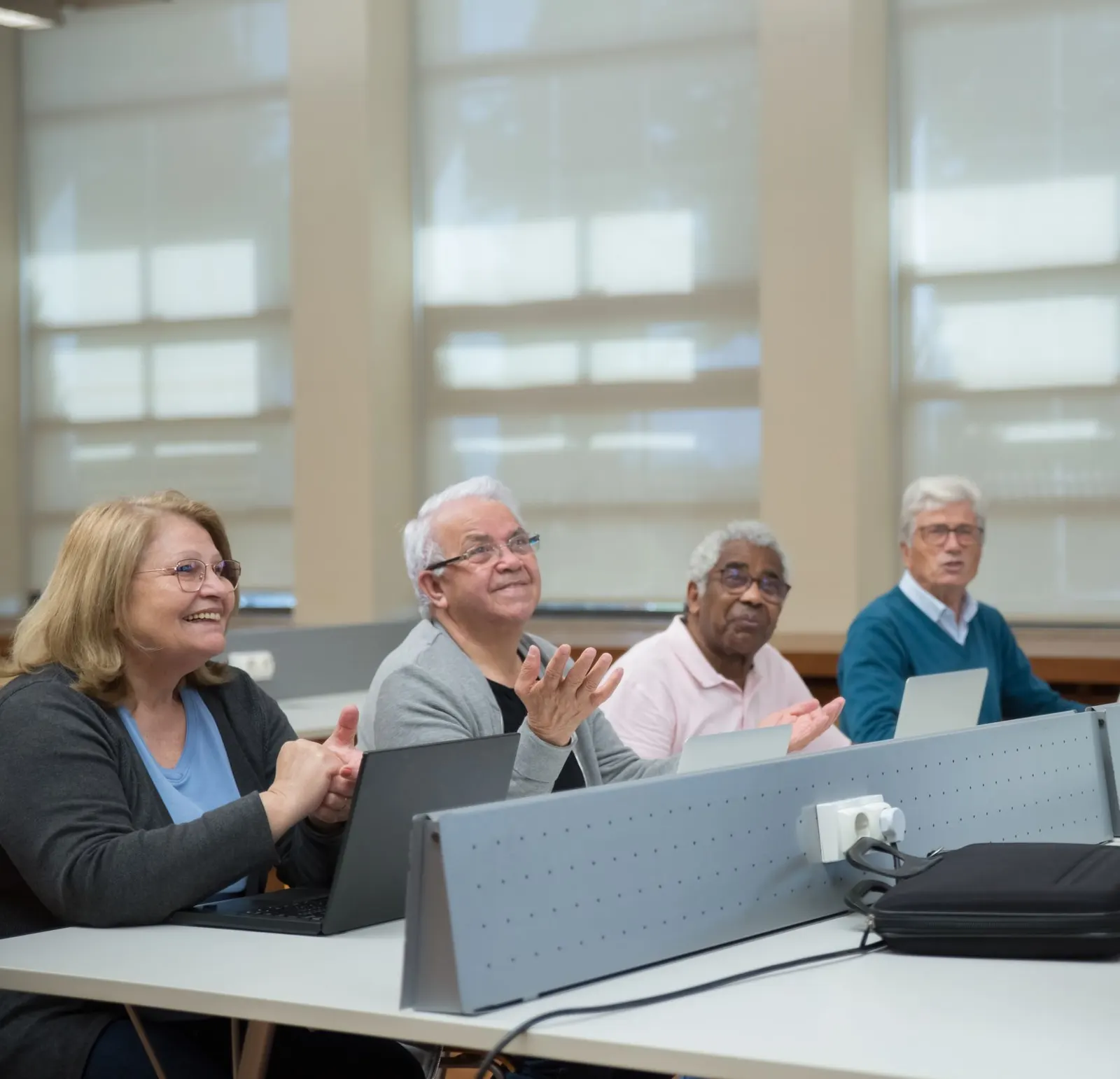 Older adults smiling and applauding during a class in a bright classroom