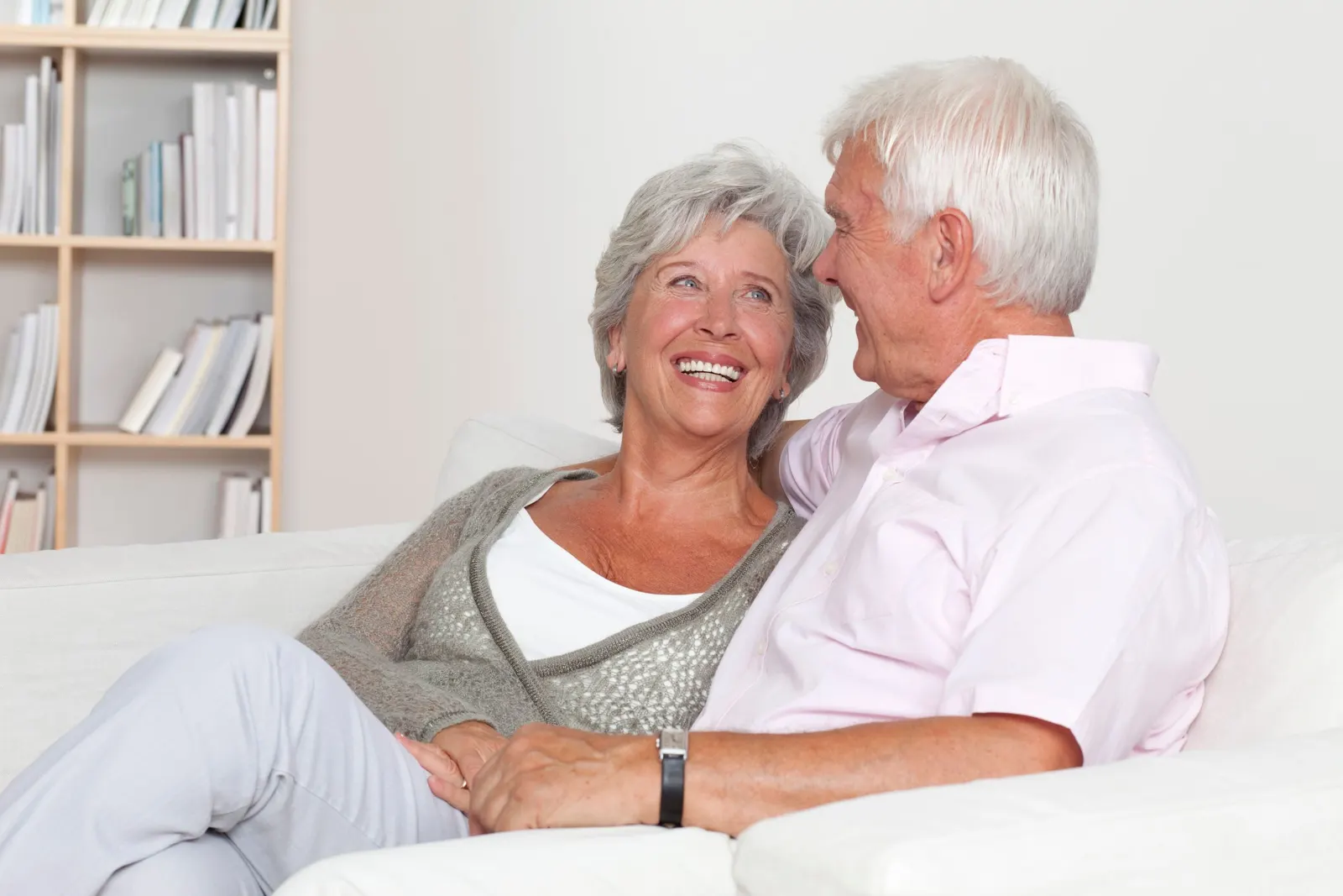 Older couple smiling together on a white sofa in a bright living room