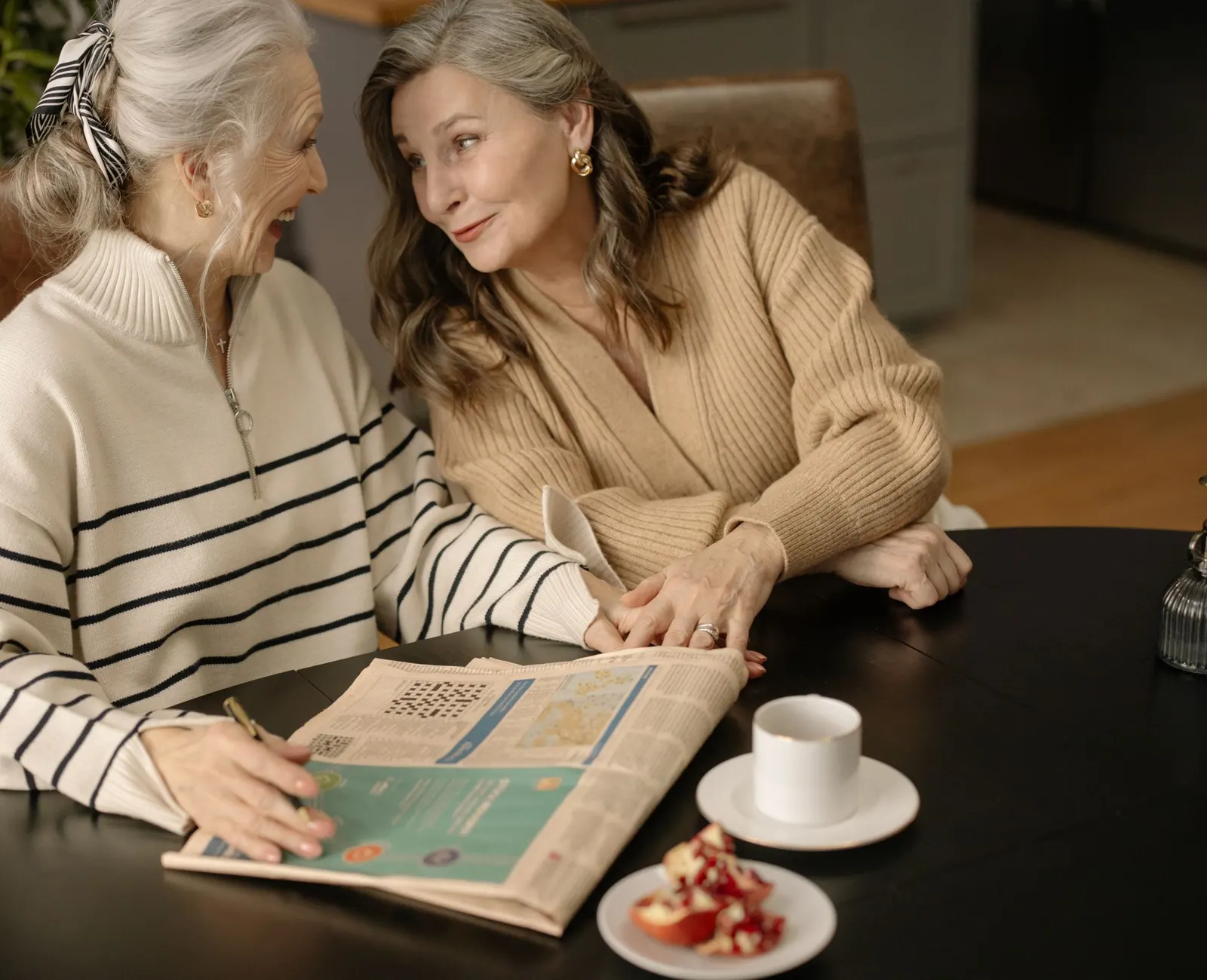 Two older women laughing together over coffee and the morning paper